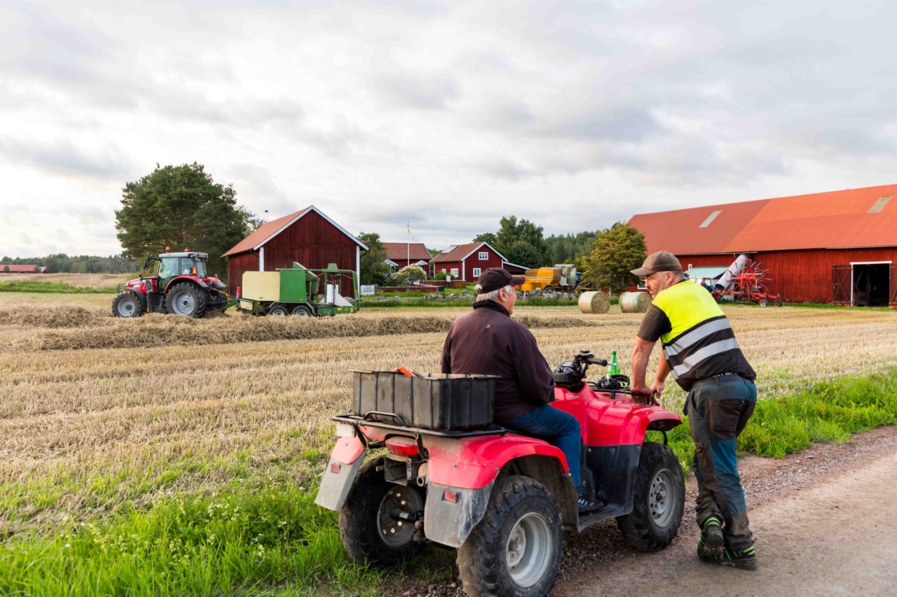 bonde står parkert med ATVen sin og prater med en venn langs veien utenfor gården