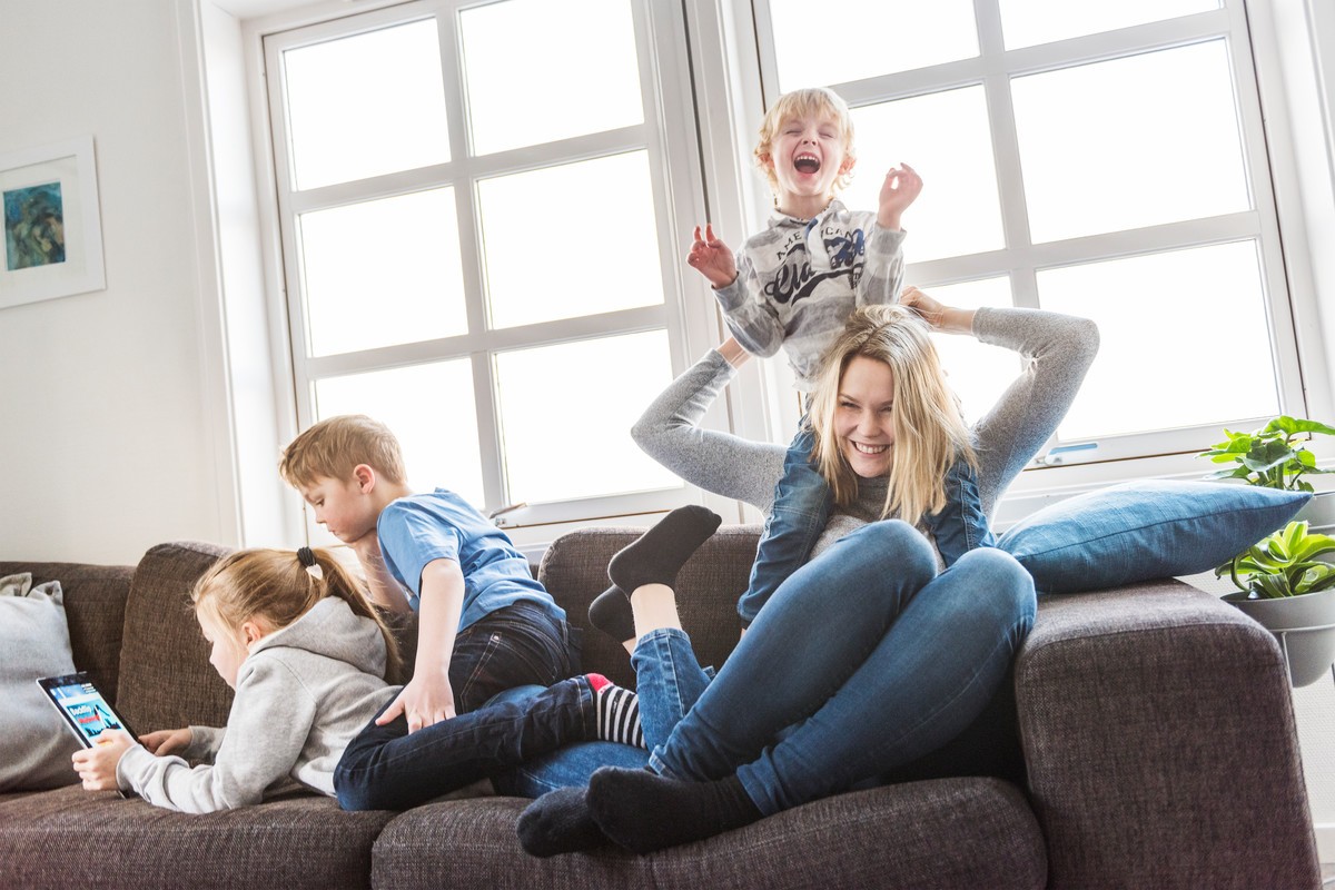 Familie med mor og tre barn leker i sofaen og ler