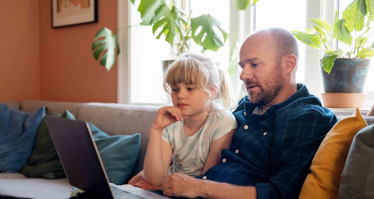 uføretrygdet far sitter med datter på fanget og ser på skjerm